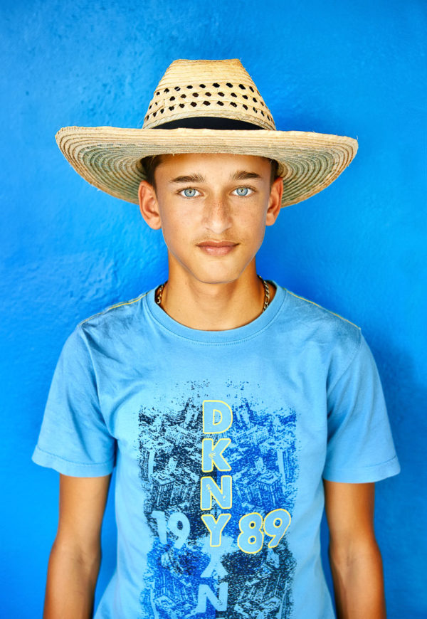 Kubanischer Junge mit Blauen Augen und Strohhut steht vor blauer Wand